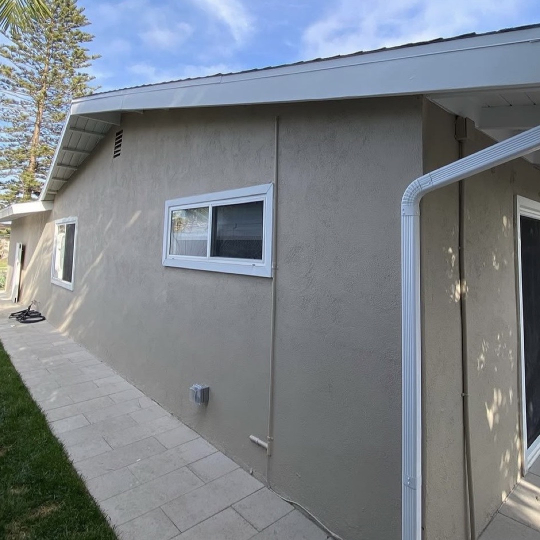 After: stucco house repainted in warm gray with white trim and gutters