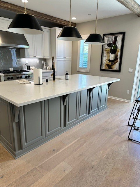 Long gray kitchen island with white counters and black pendant lights