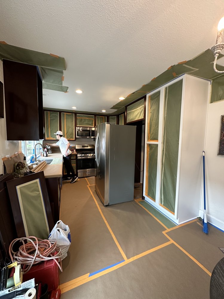 Kitchen mid-job: floor covered in paper, cabinet frames masked, a painter at work