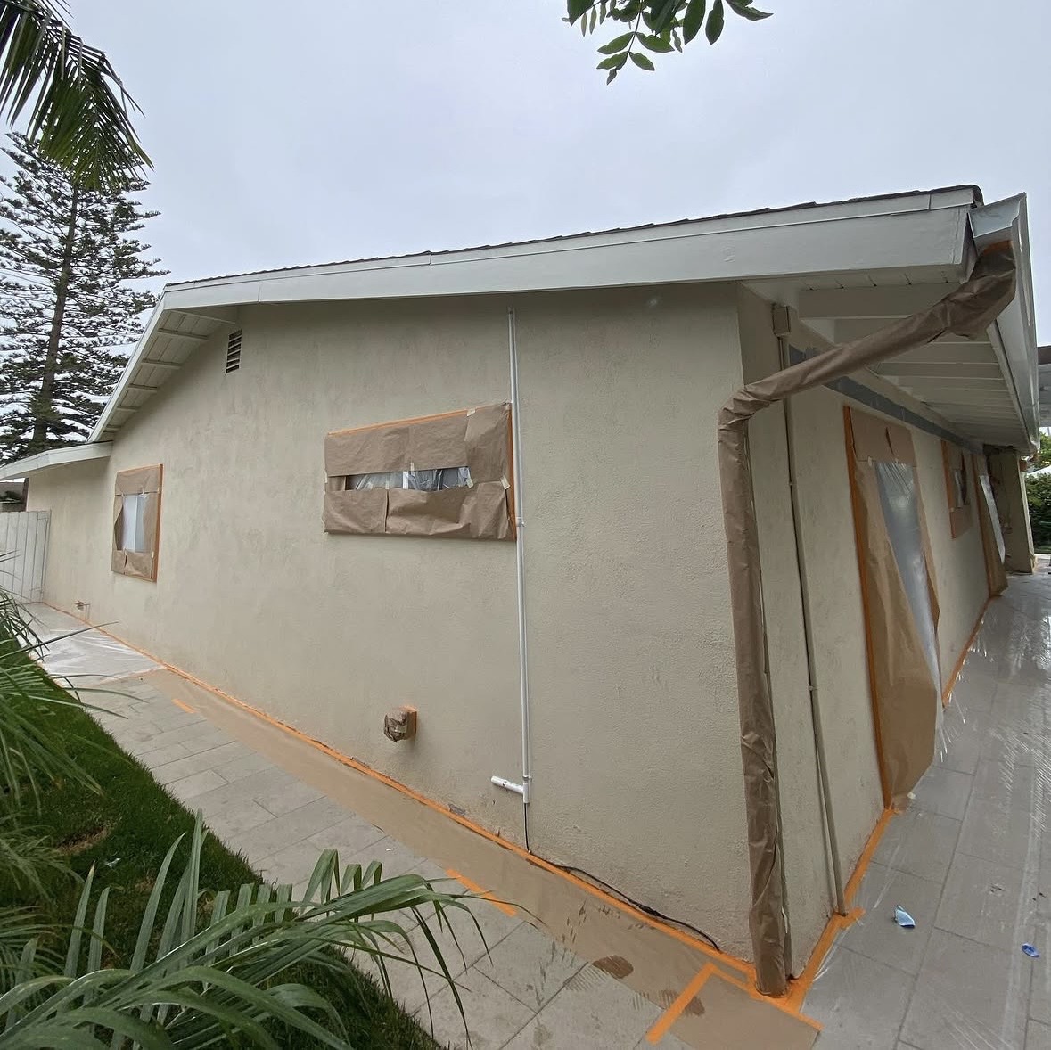 House exterior with windows and downspout wrapped in brown paper and orange tape